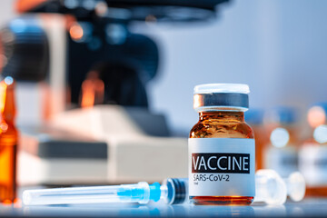 Vial of Covid-19 vaccine next to a microscope