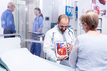 Obraz premium Physician pointing at heart disease using tablet pc and talking with patient about diagnosis. Medical services medicine healthcare well-being support, physician working