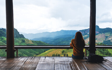 Rear view image of a female traveler sitting and looking at a beautiful mountain and nature view