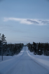 long snowy road in Lapland, Finland. Aerial drone shot of the forest covered in snow winter and the...