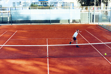 Man plays tennis on clay tennis field view from afar