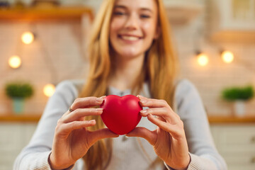 Happy young woman holding red heart, smiling and saying thank you for love and generosity