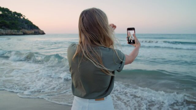 Happy beautiful young woman make selfie on smartphone at beach, laughing and smiling to camera. Travel blogger or social media influencer. Authentic emotions of happy holiday maker