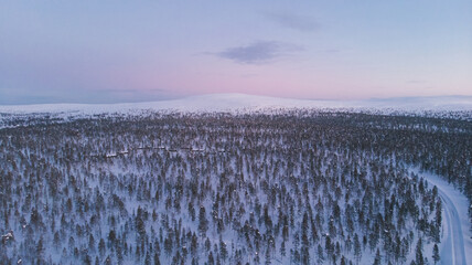 Winter sunset in Lapland, Arctic circle. Moon rising over horizon. Aerial drone shot of the forest covered in snow winter and the village inside the Arctic Circle. Lapland, Finland. Winter sunrise 