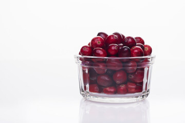 Fresh raw organic cranberry in glass bowl plate on white background with berries next to it. Space for text.