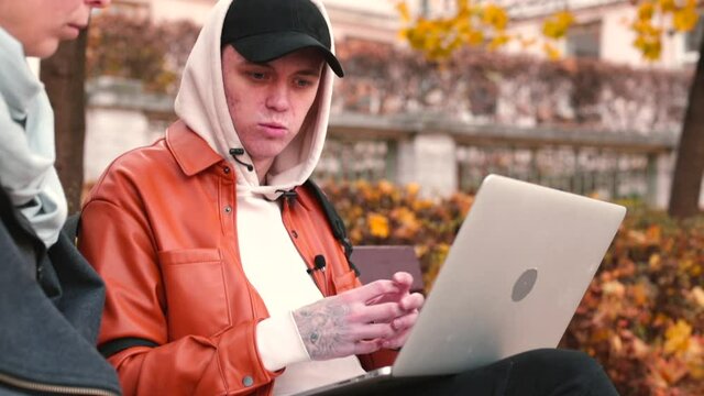 Conversation in an autumn park. The young man is gesturing, trying to explain the meaning to his interlocutor. Open laptop on lap. Confidence and assertiveness in expressing emotional intelligence.