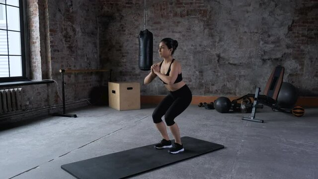 Young Indian Athletic Woman Doing Sports Doing Squat Exercise, Wearing Sportswear Black Top and Leggings, is In the Gym