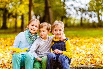 Portrait of three children hugging in autumn park. Two boys and eldrely girl in bright warm day spend time together