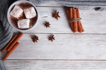 Mug of chocolate with marshmallow, spices, grey knitted scarf on white wooden table background. Winter drink concept. Spicy cocoa, menu, top view, copy space