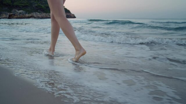 Camera follows woman walk barefoot on beautiful calm sandy beach at resort or hotel. Ocean waves surf roll over her feet. Concept tranquility and self care in peaceful setting