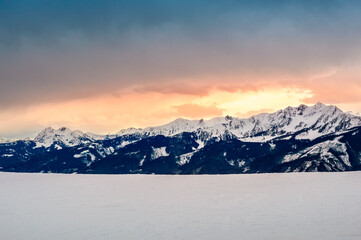 Fototapeta na wymiar Zell am See in winter. View from Schmittenhohe, snowy slope of ski resort in the Alps mountains, Austria. Stunning landscape with mountain range, snow and sunset sky near Kaprun