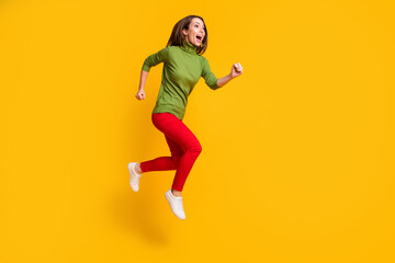 Fototapeta na wymiar Full size photo of funny lady jump up rushing excited wear casual green pullover shoes red trousers isolated yellow color background