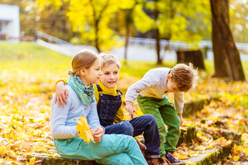 Three children sitting on old leafy stairs in autumn park. Two blond children sitting together on...