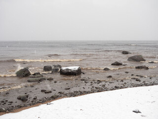 Strong waves on Lake Onega in the Republic of Karelia, rocky lake shore covered with the first snow