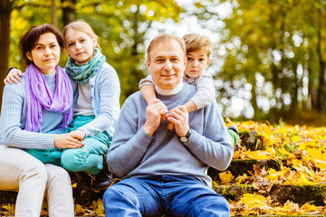 Fototapeta premium Happy family in the park for a walk in the summer, in the fall. Mother, father and two children walking on nature. Parents and children smile, laugh, play in the afternoon.