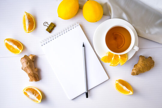 Trendy flat lay Ginger hot immunity boosting Vitamin natural drink With citrus lemon notebook and pencil on white background. Copy space