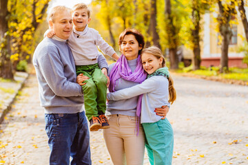 Fototapeta premium Happy portrait family of four walking in autumn city park. Children and parents posing, hugging, smiling, playing and having fun. Bright yellow trees.