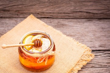 Honey in a glass jar with lemon on wooden background