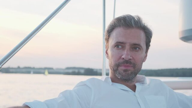 Portrait of handsome man on the yacht. Close up of confidence man on sailing boat at sunset in marina.