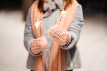 Christmas sparkles in hands. Cheerful young woman celebrating holding sparkles in the winter forest. Festive garland lights. Christmas, new year.	