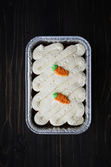 Carrot cake and cream cheese in an aluminium container. Wooden background.