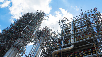 Obraz premium Distillation tower or column on blue sky with clouds background. Oil refinery plant. Refining complex. Petrochemical industry concept.