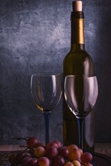 A beautiful still life with wine glasses, a bunch of grapes and a bottle of wine. Calm muted colors. Vertical arrangement