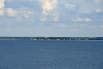 View of the Polish sea with some land in the distance and some reeds or shrubs growing next to the sandy coast of the reservoir seen on a cloudy yet warm day on a Polish countryside next to a resort