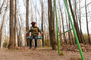 A young toddler boy swinging on a swing in forest. Front view. Selective focus.