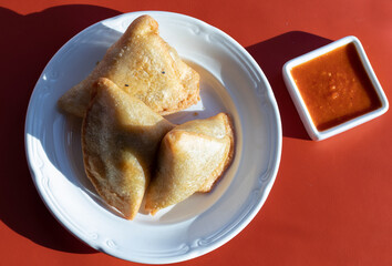Samosas on a white plate and red sauce on a red background, high shadow contrast, top view