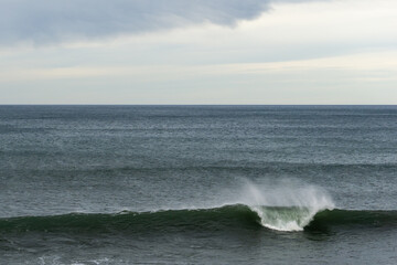 large wave breaking in the ocean with copy space and blue and cloudy sky