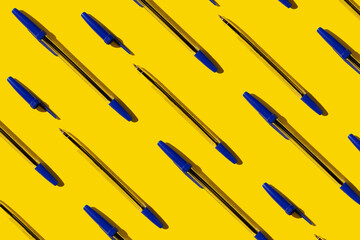 blue plastic pens on a bright yellow background. geometric pattern on the theme of office and...