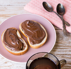Spread chocolate-nut cream on slices of bread with a Cup of tea. Delicious Breakfast with chocolate and nut paste and a Cup of tea.