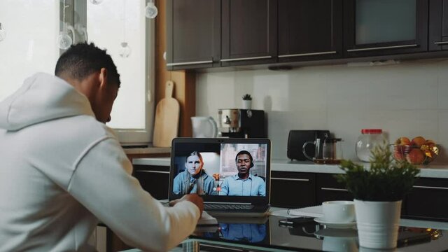 Multiracial colleagues working home on quarantine by making common video call by computer. Black man sitting in the kitchen and writing.