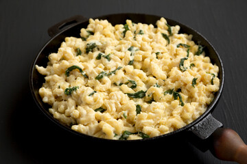 Homemade Spinach Mac and Cheese in a cast-iron pan on a black background, side view. Close-up.