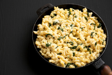 Homemade Spinach Mac and Cheese in a cast-iron pan on a black background, side view. Space for text.