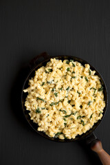 Homemade Spinach Mac and Cheese in a cast-iron pan on a black background, top view. Flat lay, overhead, from above. Copy space.