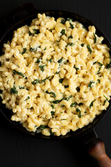 Homemade Spinach Mac and Cheese in a cast-iron pan on a black surface, top view. Flat lay, overhead, from above. Close-up.