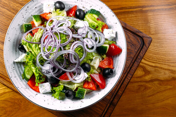 Fresh greek salad with tomato, cucumber, bel pepper , olives and feta cheese on black plate, top view, on the wood 