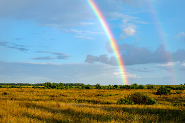 Rural landscape with a rainbow on a light sky with clouds in the countryside on a summer day