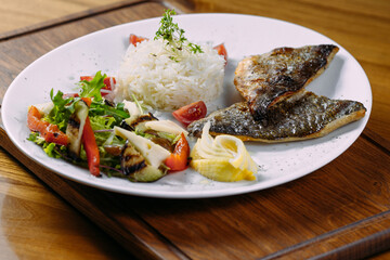 dorado fish fillet with garnish on a plate and wooden table
