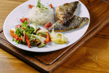 dorado fish fillet with garnish on a plate and wooden table