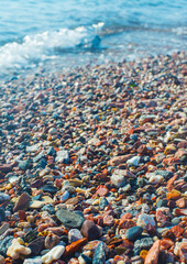 Bright wet pebbles on the coast in the foam of the surf