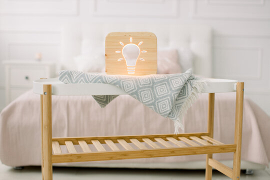Wooden lapms and decor details at home interior. Stylish wooden hand made lamp with electric light bulb cut out picture, on little coffee table, standing in light home bedroom