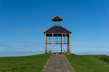 simple gazebo pavillion with stone walkway in a green meadow under a blue sky