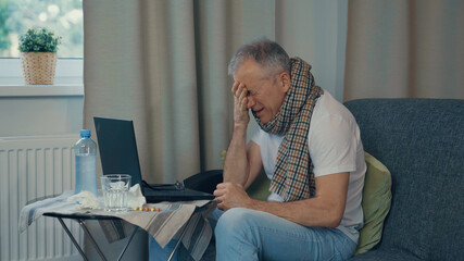 A man gets sick, sneezes and coughs while working at the computer.