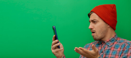 Close up portrait of hipster young model with looking at smartphone isolated on green background. Looking and surprised.