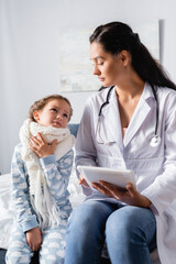 Obraz premium ill girl touching sore throat and looking at doctor holding digital tablet