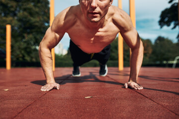 Young shirtless man bodybuilder doing push-ups on a red rubber ground during his workout in a modern calisthenics street workout park