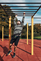 Young man bodybuilder exercising on monkey bars during his workout in a modern calisthenics street...